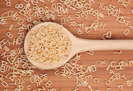 Wooden spoon with alphabet shaped pasta spread around it